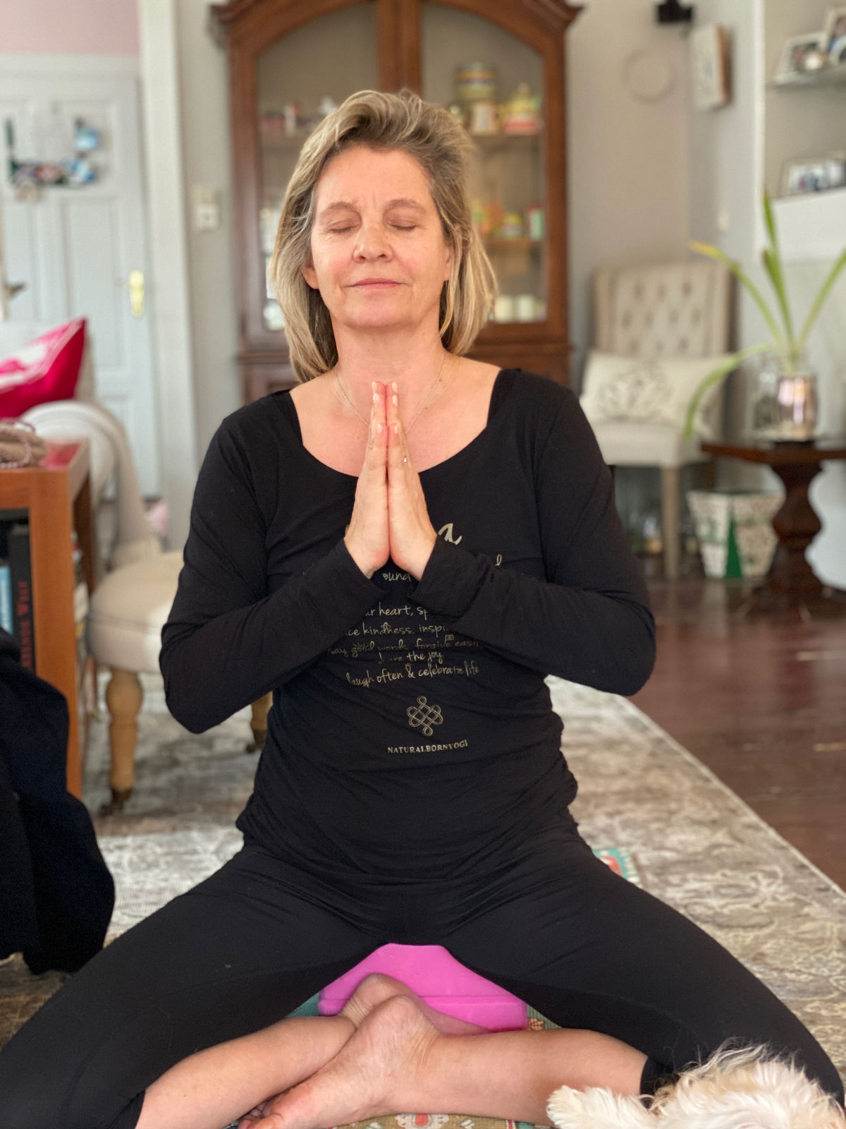 Yogalehrerin meditiert im Schneidersitz in ihrem Wohnzimmer